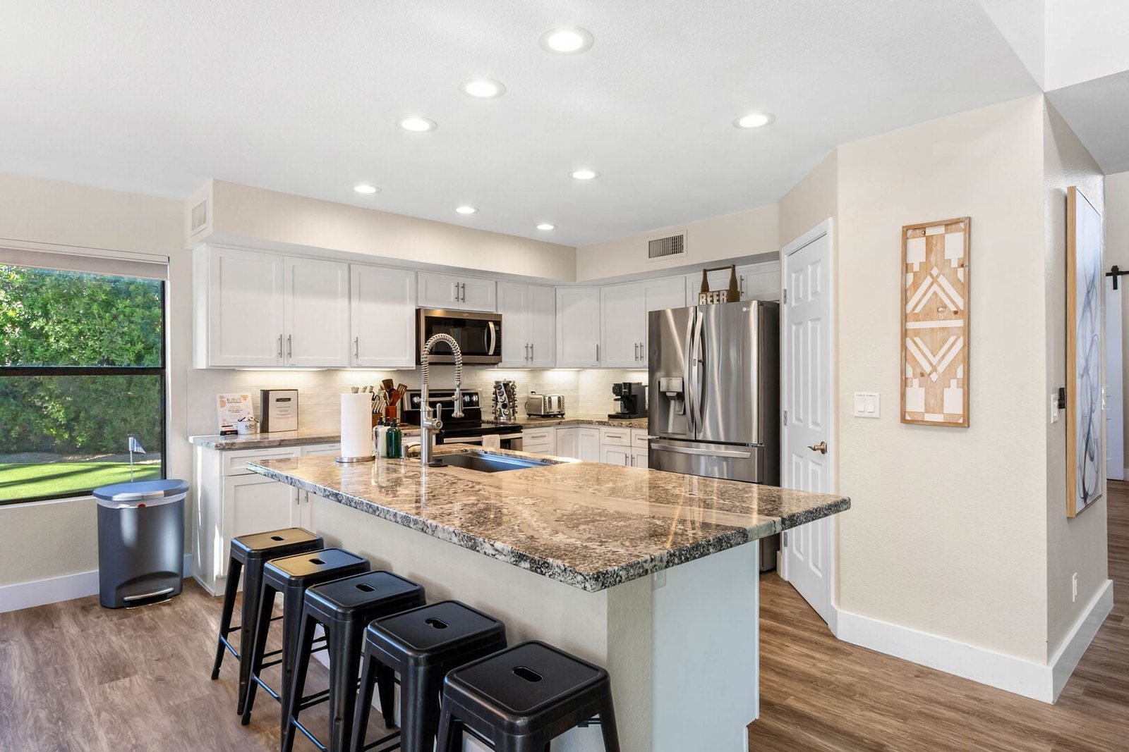 Remodeled kitchen with white cabinetry, granite island and bar stools