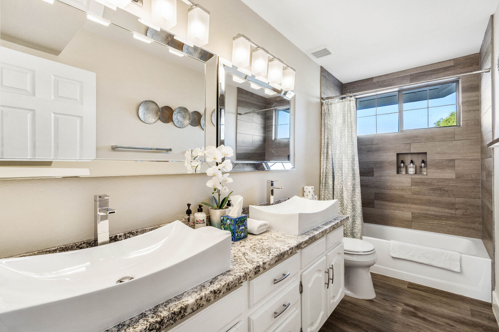 Guest bathroom with double vessel sinks, granite counter and wood-look tiled tub surround