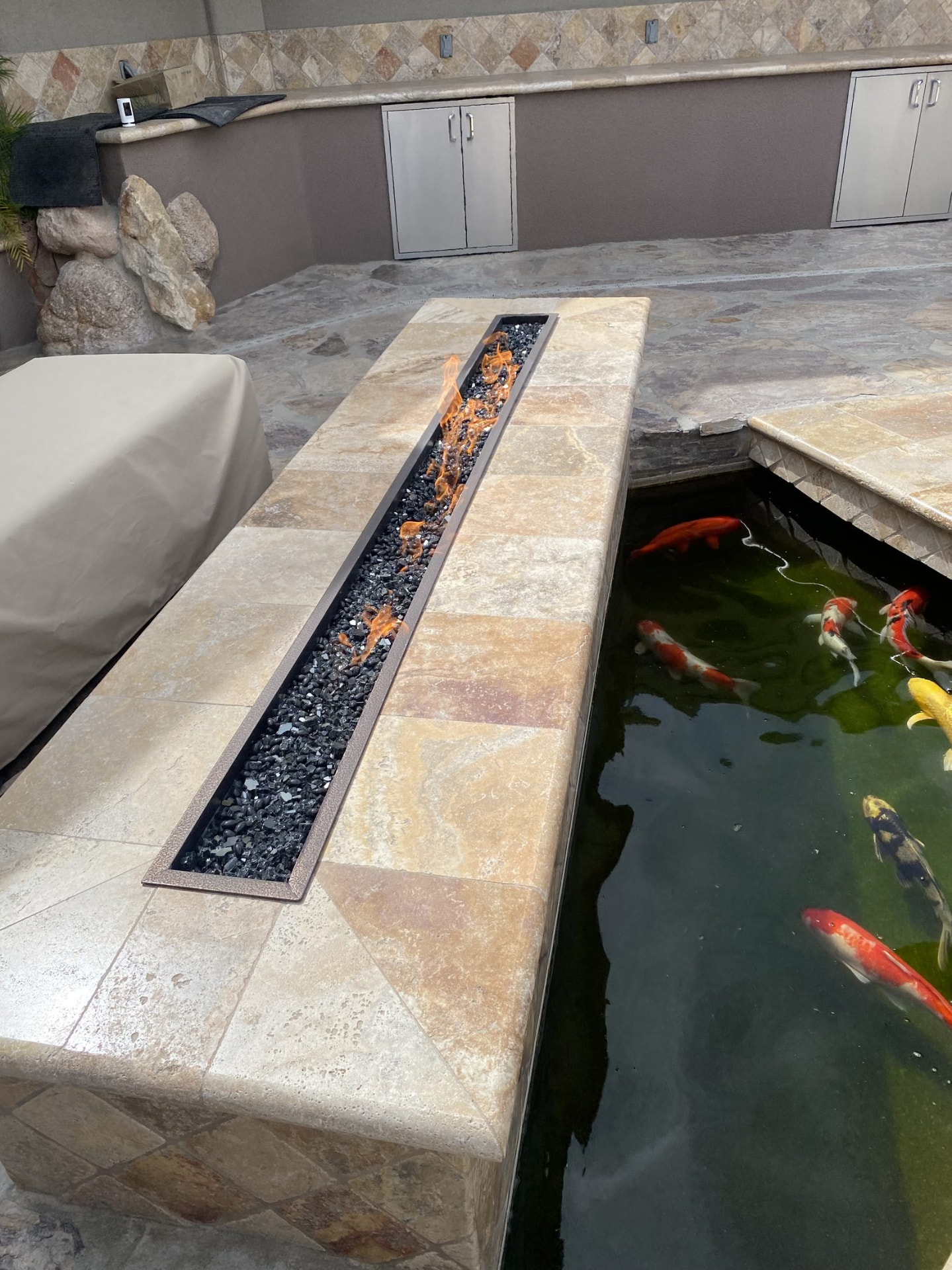 Close view of a linear fire feature beside koi swimming in dark water
