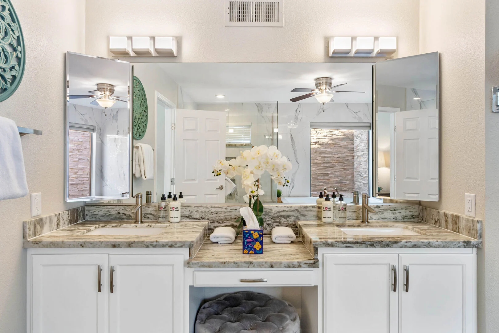 Primary bathroom double vanity with stone counters, white cabinetry and mirrored cabinets